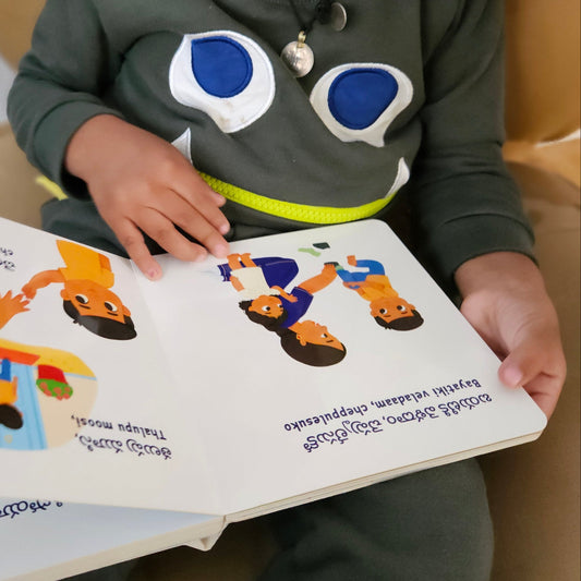 Child reading a Em Cheddaam Eeroju telugu board book with colorful illustrations.