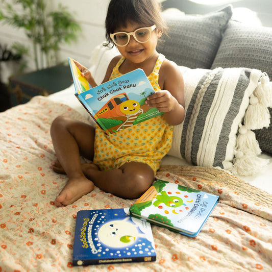 Child reading chuk chuk railu on a couch with other books around like chitti chilakammaa and chandamaama raave