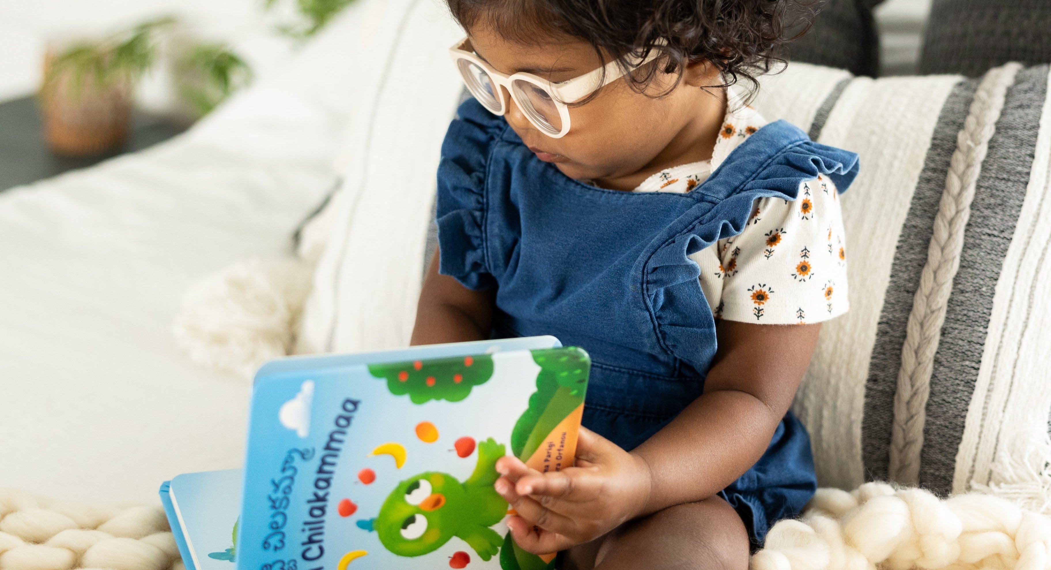 Child reading a book on a cozy couch with plants in the background