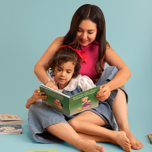 A woman and a young girl sit together reading Raajugaaru Edu Chepalu, a Telugu-English board book by Bhaalu Books